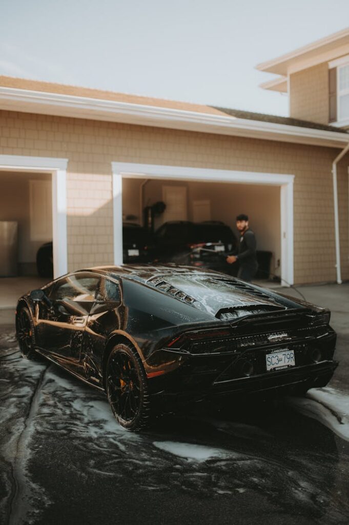 A sleek Lamborghini sports car getting washed in a driveway with a person nearby.